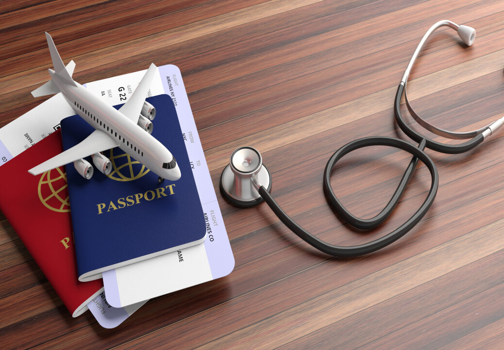 Passport, boarding pass, a model plane and a stethoscope on a desk